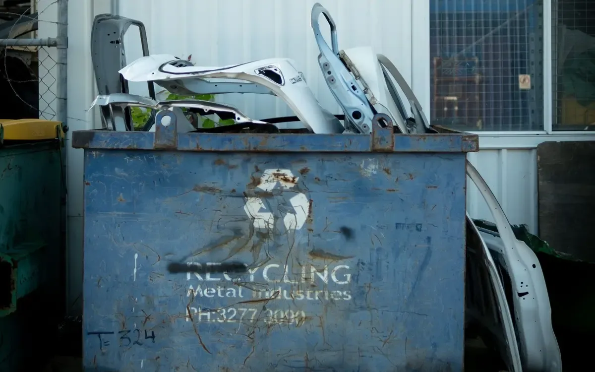 A scrap metal bin filled with panels standing beside a workshop wall.